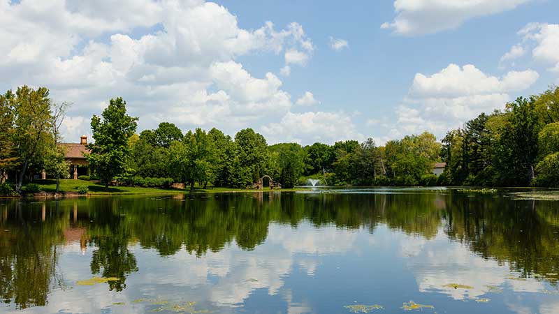 A peaceful summer view of the lake at Gervasi Vineyard in Canton, Ohio, reflecting blue skies and lush trees, offering a tranquil backdrop for outdoor wine experiences.