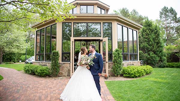 Bride and groom kissing in front of the Conservatory at Gervasi Vineyard, a modern glass greenhouse-style venue perfect for intimate wedding ceremonies