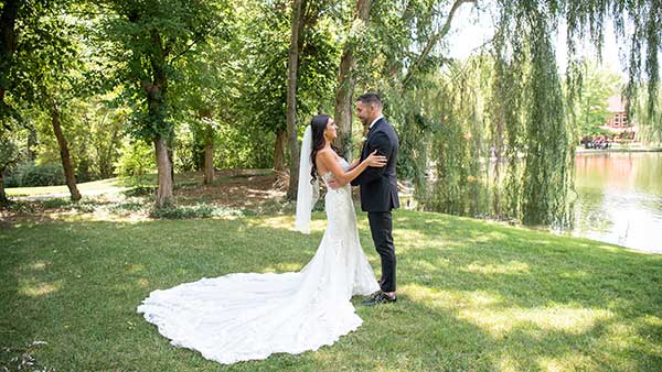 Bride and groom sharing a moment near the lakeside at Gervasi Vineyard surrounded by willow trees and greenery