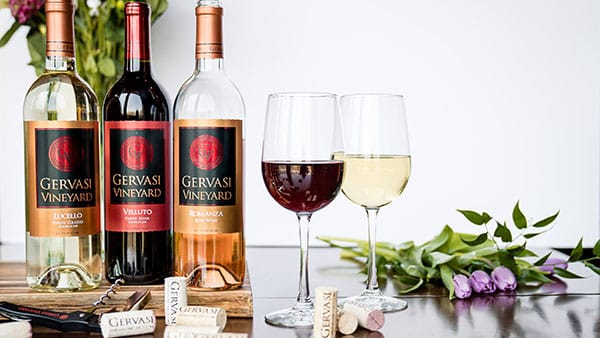 Gervasi Vineyard Lucello, Velluto, and Truscano wines with filled glasses and corks arranged on a table with flowers.