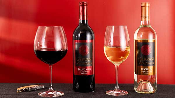 Gervasi Vineyard Truscano Sangiovese and Lucello Pinot Grigio wine bottles with filled glasses against a red backdrop