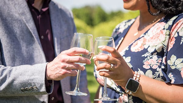 Close-up of couple clinking glasses of white wine in a vineyard setting, celebrating seasonal Gervasi wines and romantic outdoor experiences.