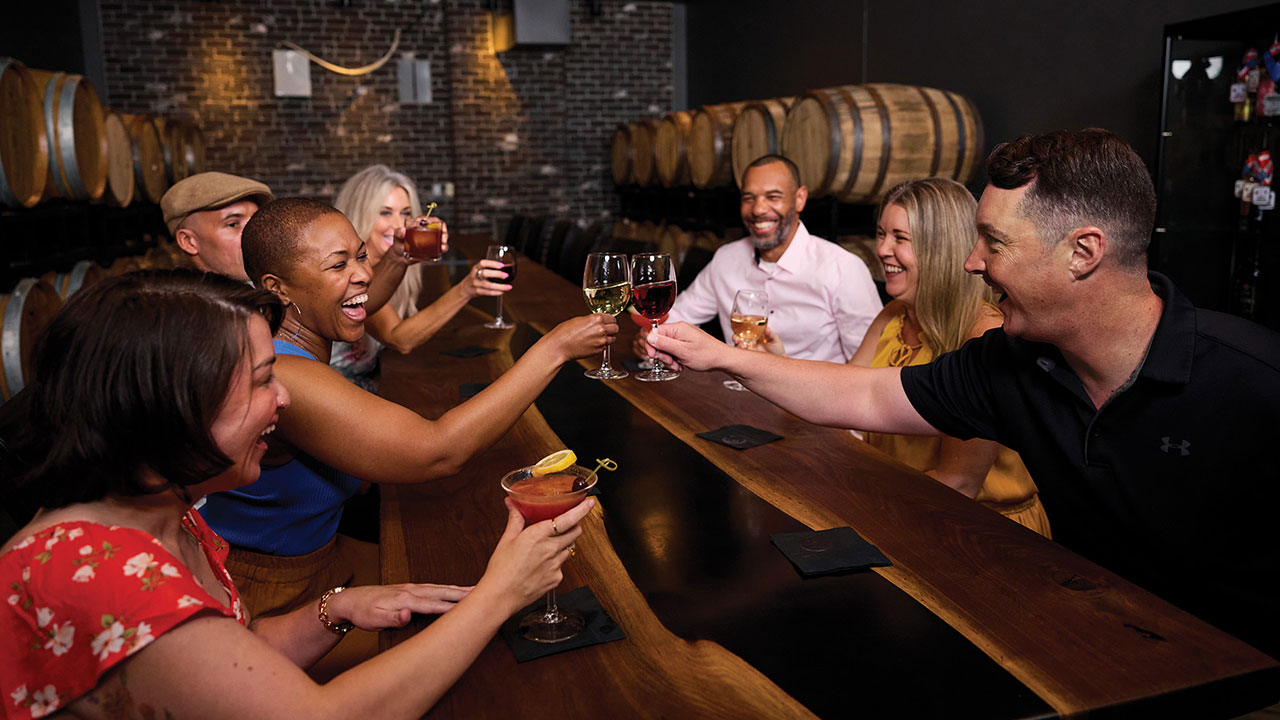 Group of friends toasting wine and cocktails inside Gervasi Vineyard’s barrel room, celebrating the season with lively conversation and handcrafted drinks.