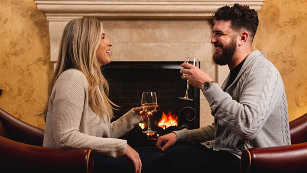 Couple enjoying wine and laughter by a warm fireplace at Gervasi Vineyard, perfect for a winter date night